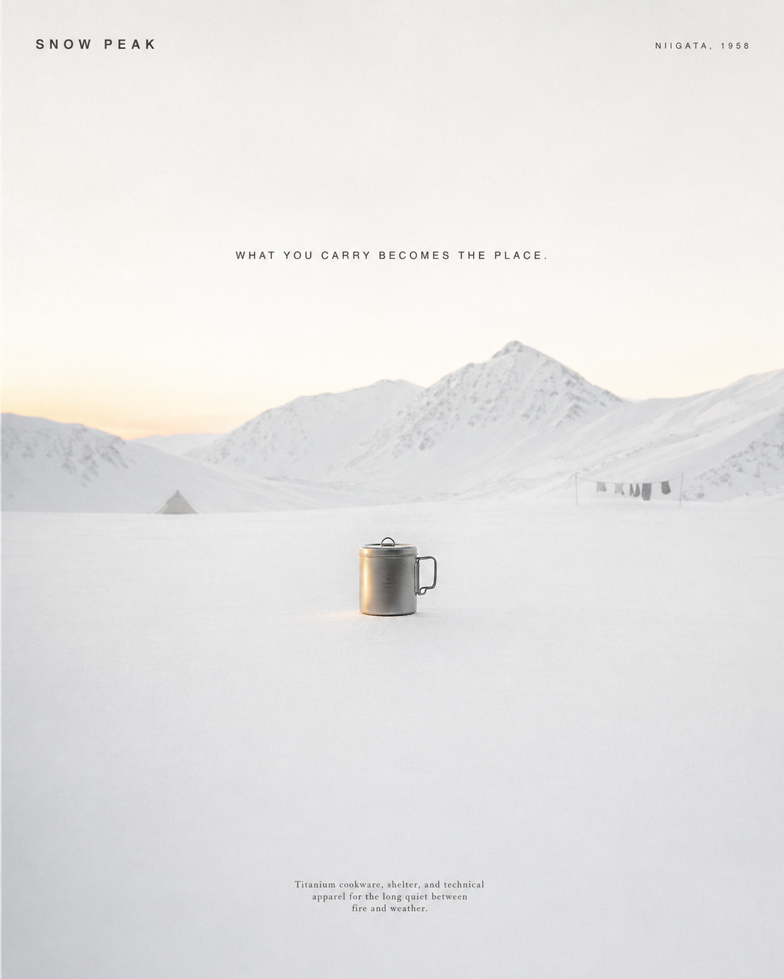 A titanium camp mug standing alone in deep snow, distant blue mountains at dawn